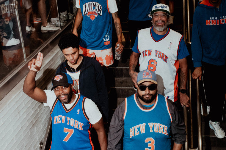 Group of people wearing New York Knicks jerseys on a staircase.