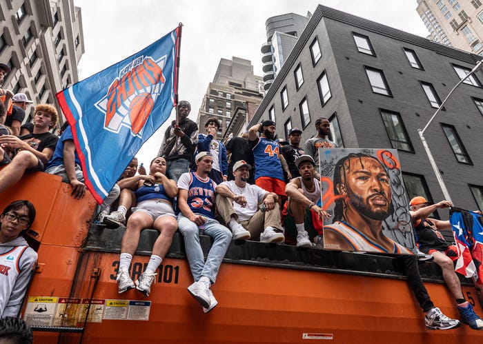 People sitting on a truck with a large painting of a basketball player, holding a flag, in an urban setting.
