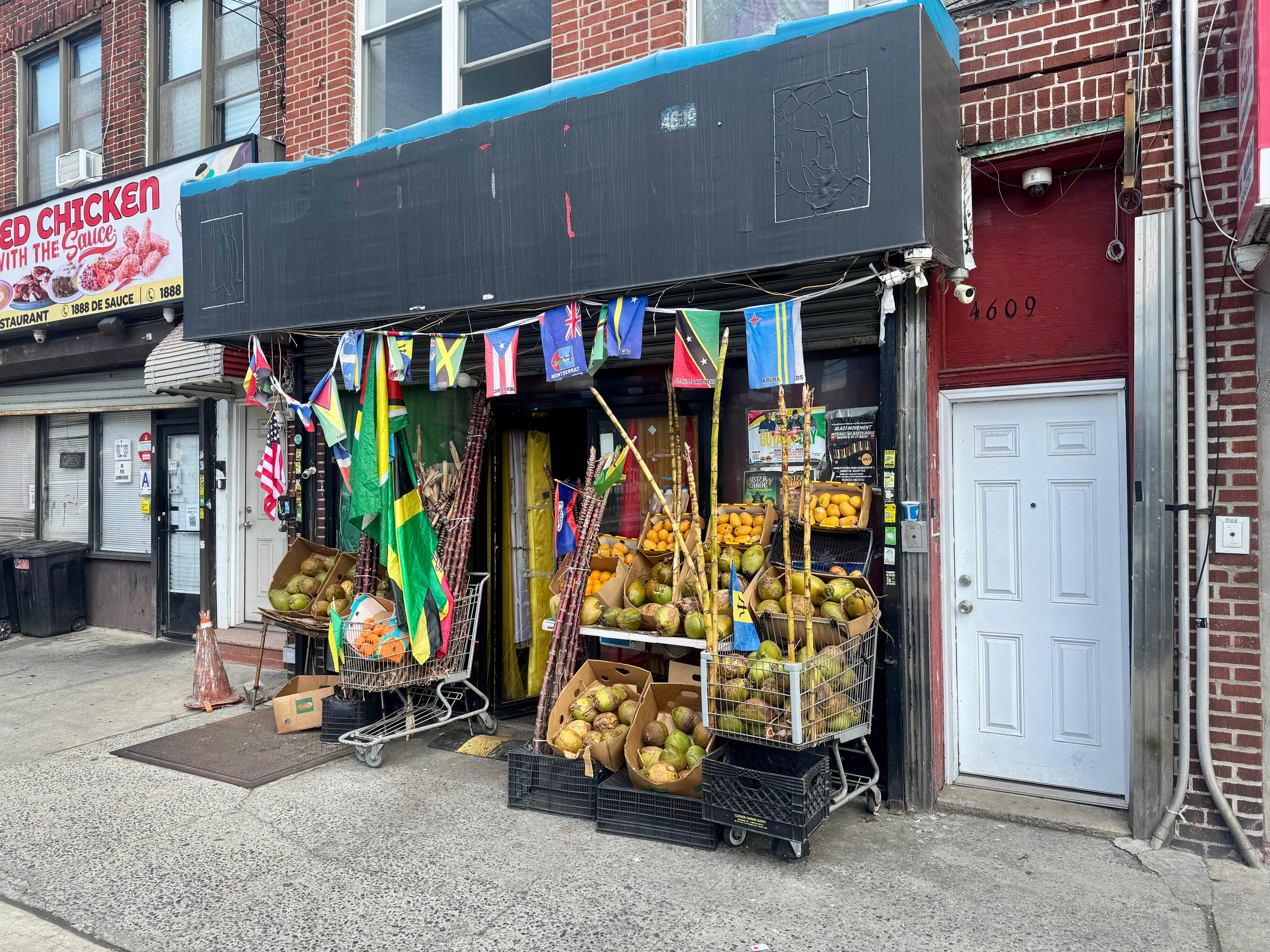 Street view of a small store with fruit displays and international flags on a brick building.
