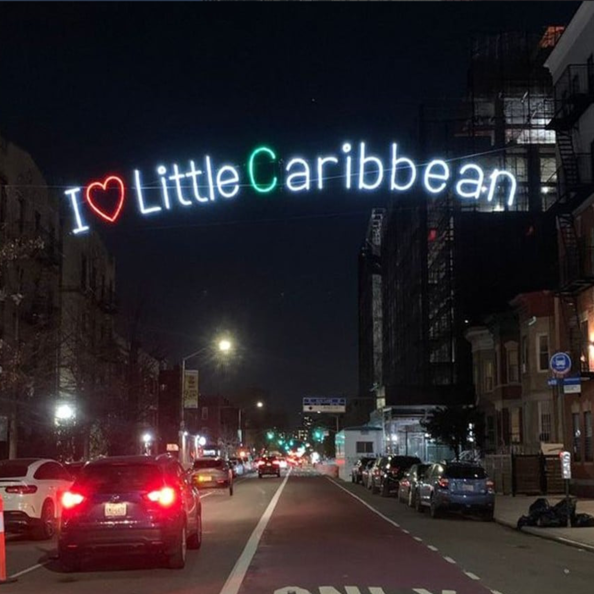 Neon sign 'I ❤️ Little Caribbean' on a city street at night.