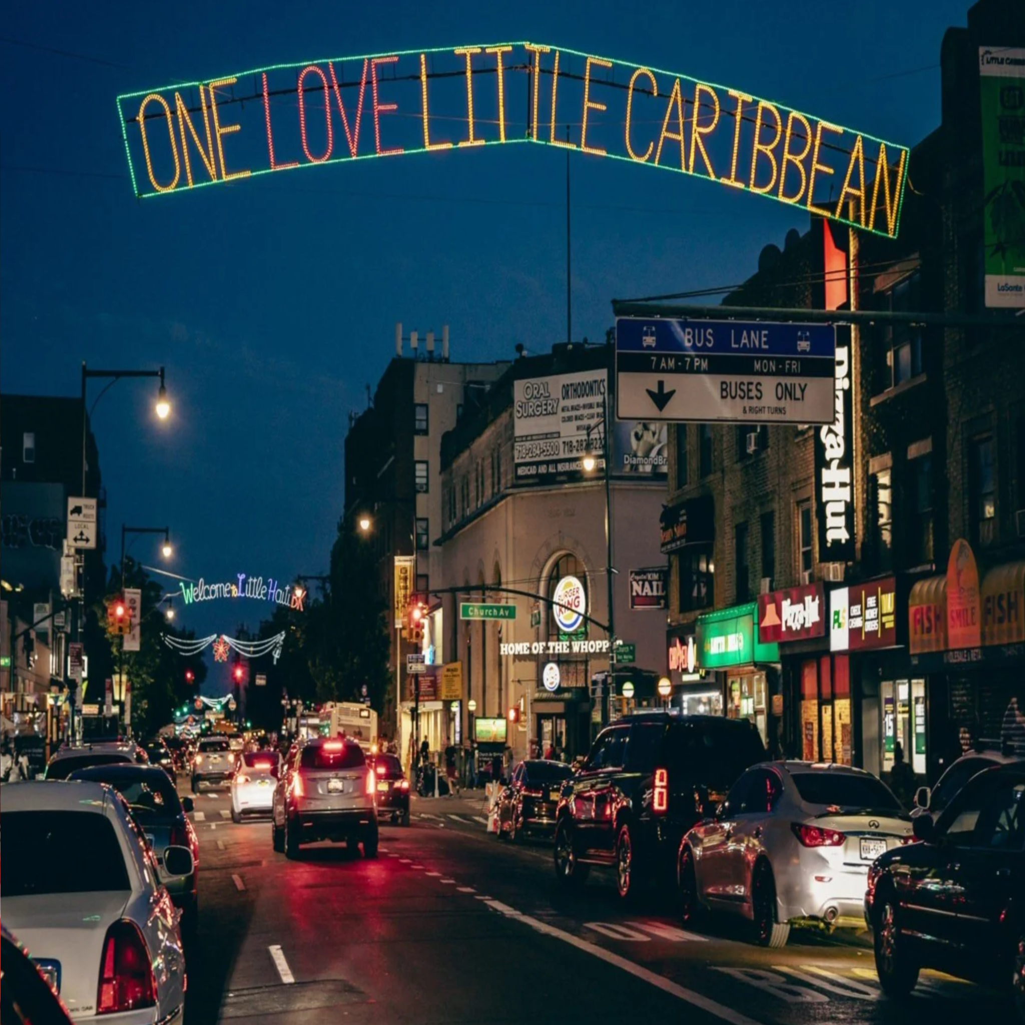 Street scene with 'One Love Little Caribbean' sign over a busy street at night.