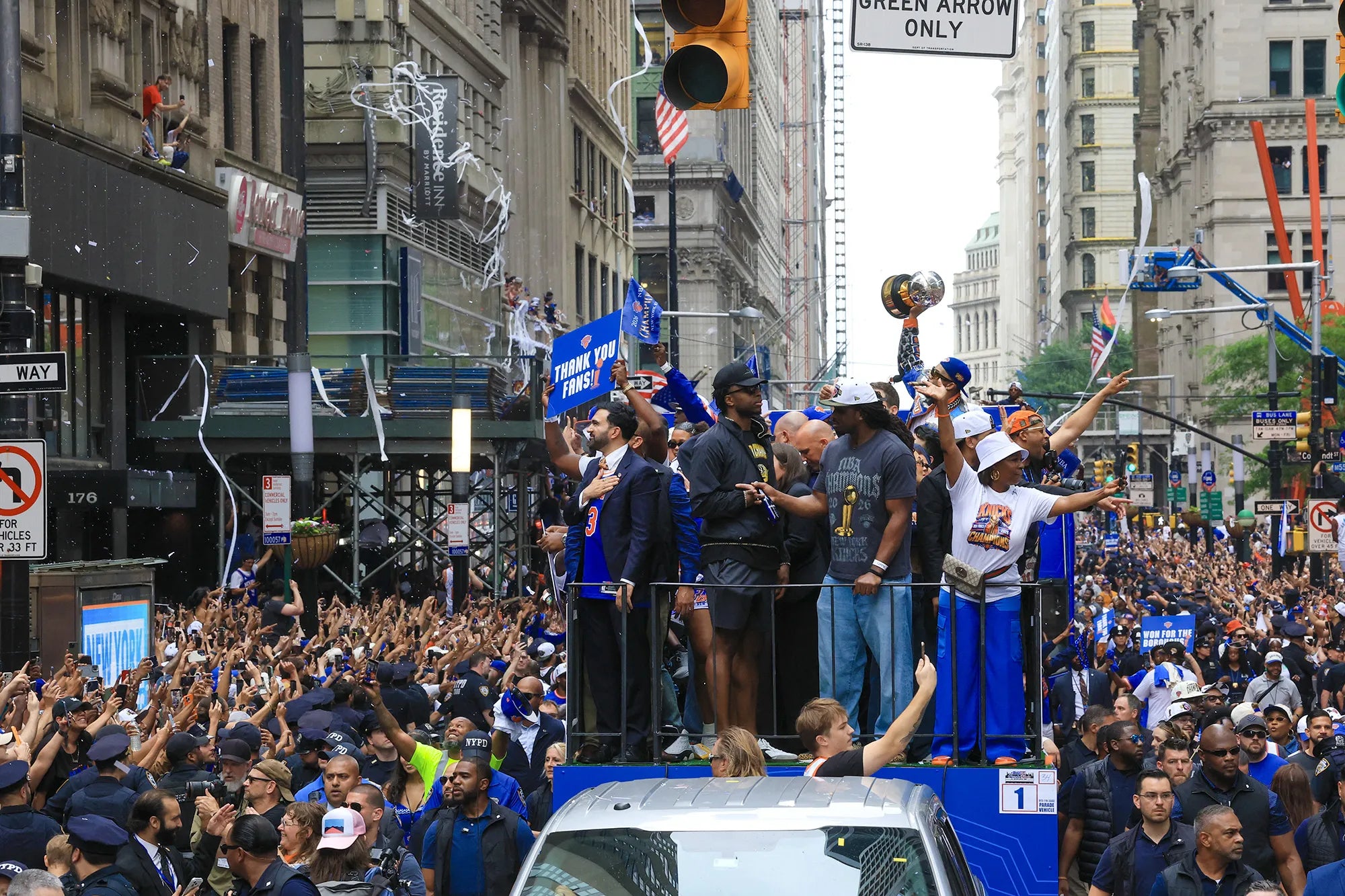 Celebration scene with people on a float holding trophies and flags in a city street.