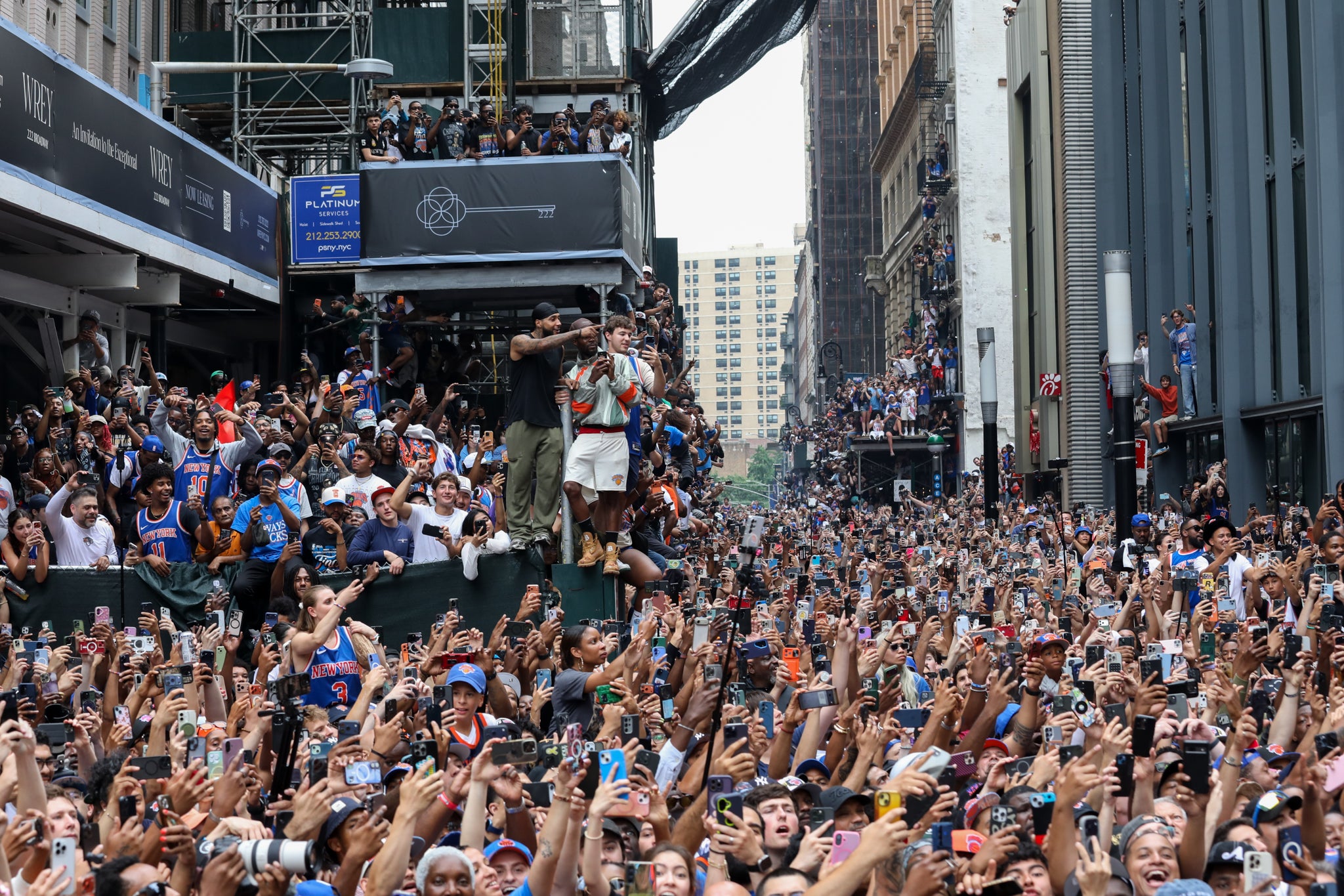 Massive crowd gathered in an urban setting for a public event, with people holding up phones to capture the moment.
