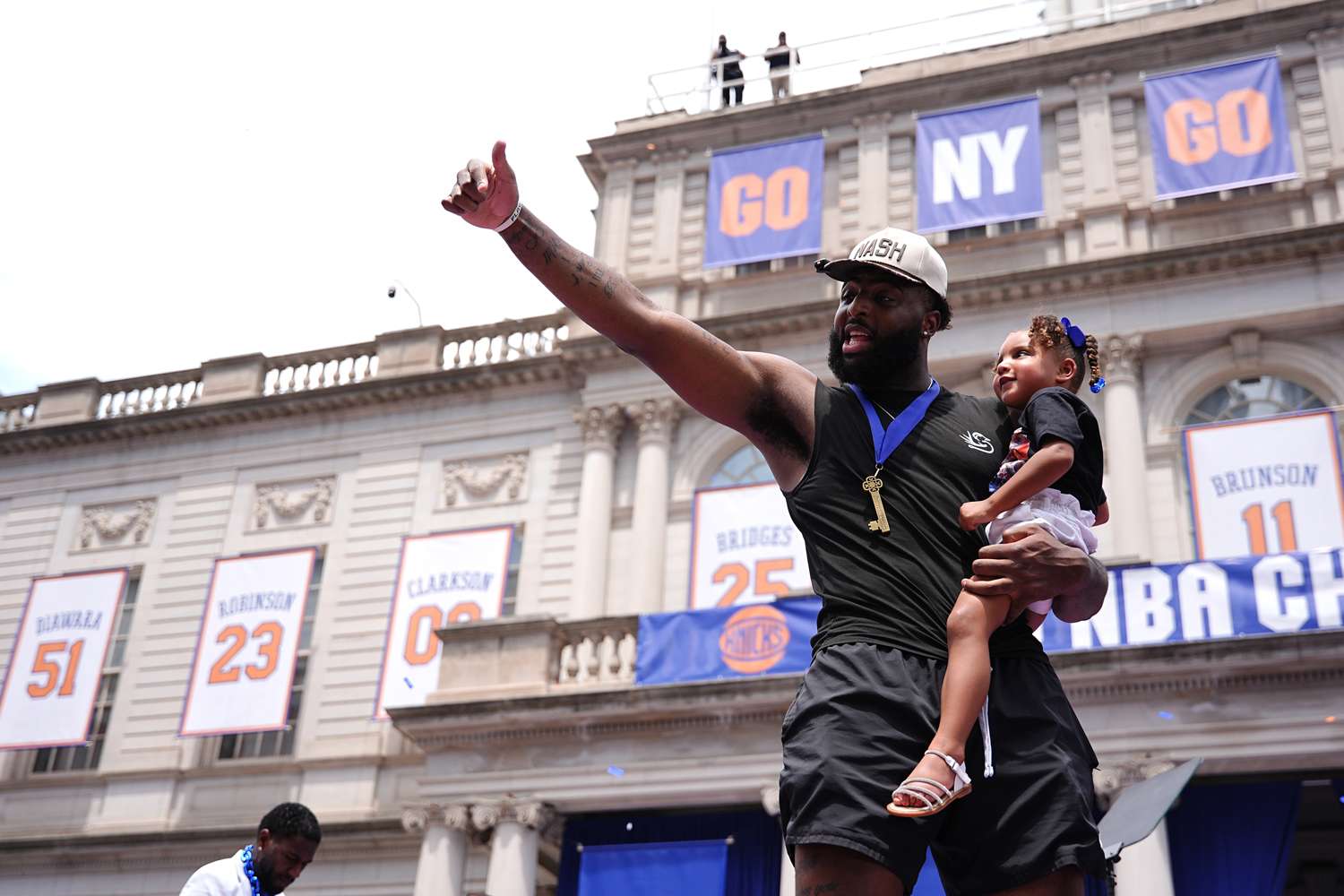 Man holding a child in front of a building with sports team banners